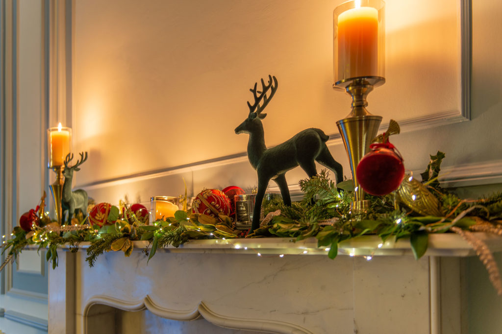 Christmas decorations on white mantlepiece with garland and candles